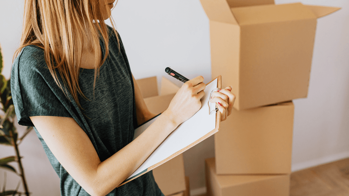 Woman writing a storage inventory checklist next to moving boxes